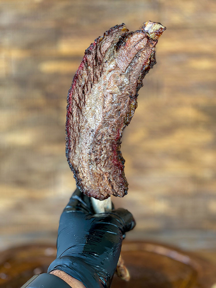 holding a single smoked beef short rib in a black gloved hand