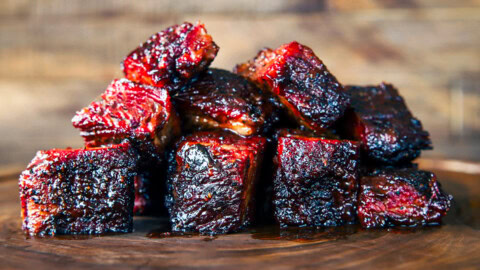 Pile of smoked brisket burnt ends with a glossy bark and sticky barbecue sauce on a wooden board.