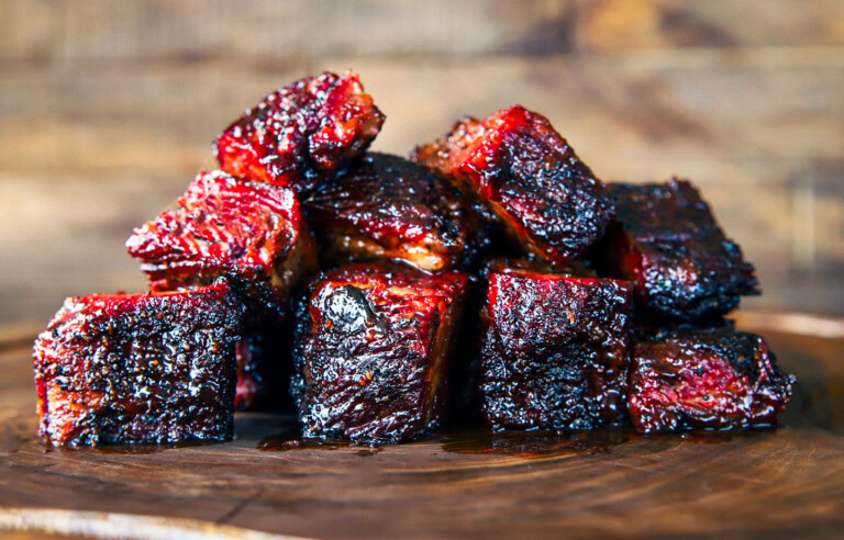 Pile of smoked brisket burnt ends with a glossy bark and sticky barbecue sauce on a wooden board.