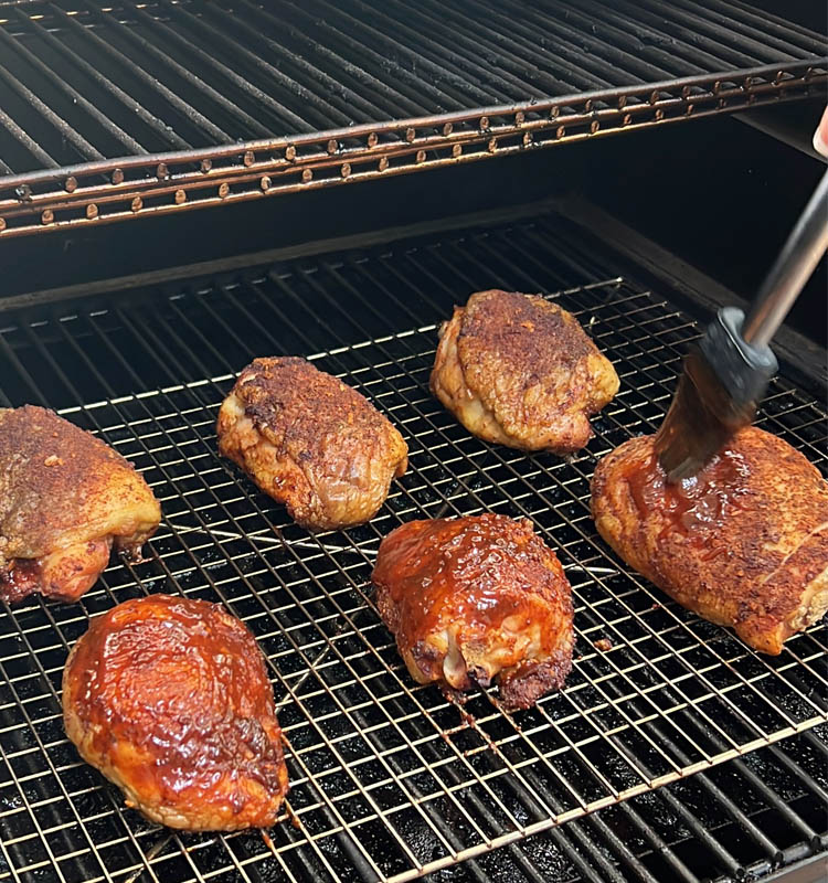 cooked chicken thighs in the smoker being basted with brush