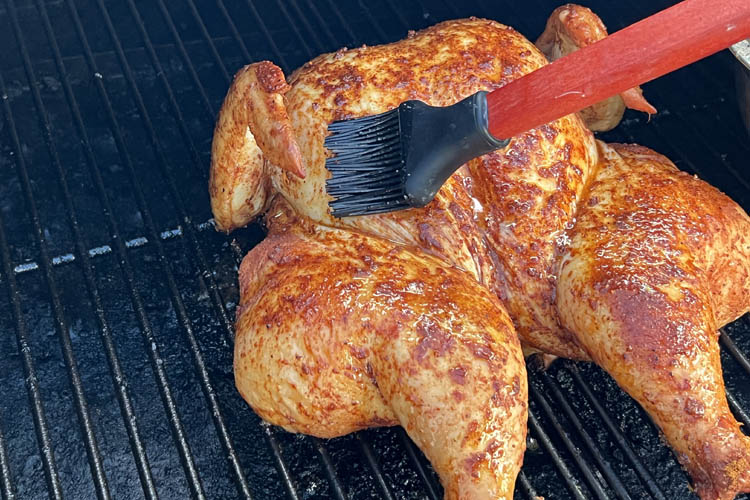 spatchcock chicken on grill being basted with a brush