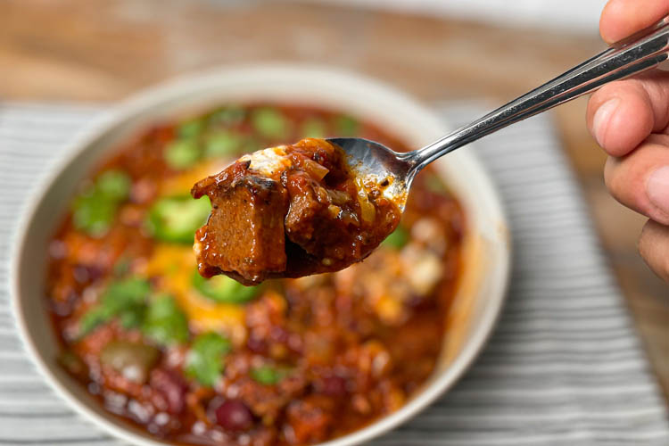 a bowl of chili in the background, spoon with chili in forground