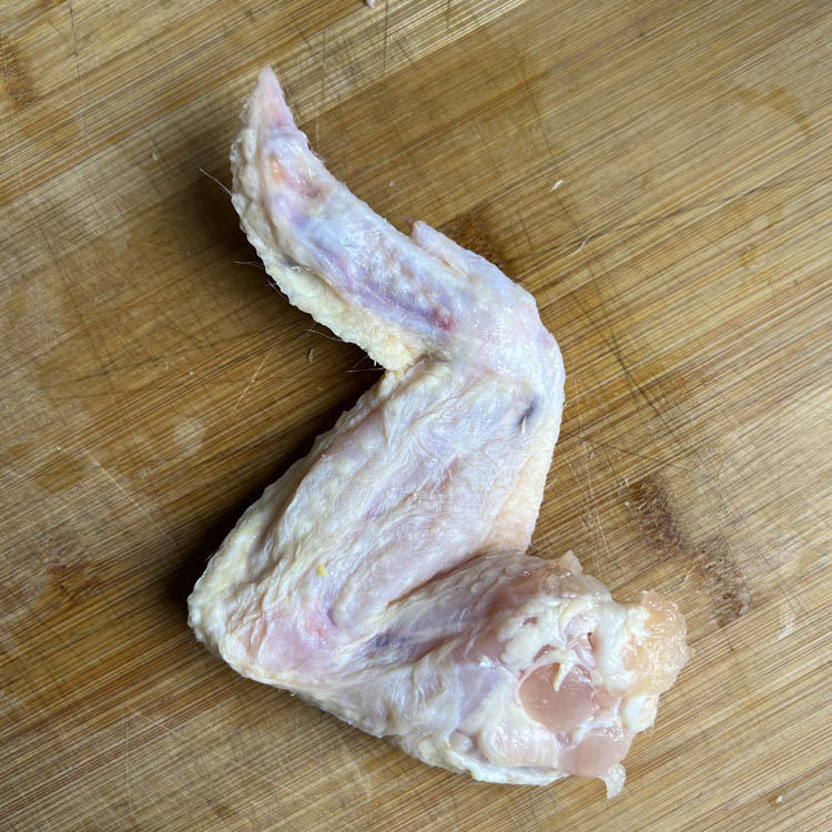 whole raw wing on wooden chopping board
