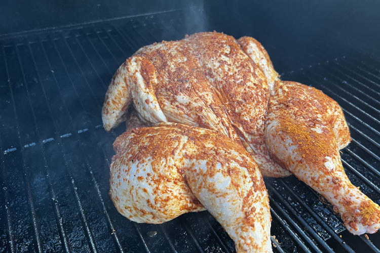 raw, seasoned spatchcock chicken on the grill