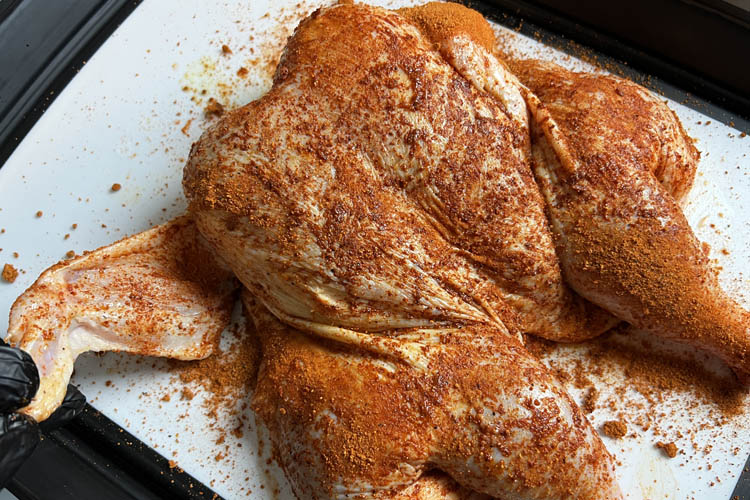 raw spatchcocked chicken with rub on white plate