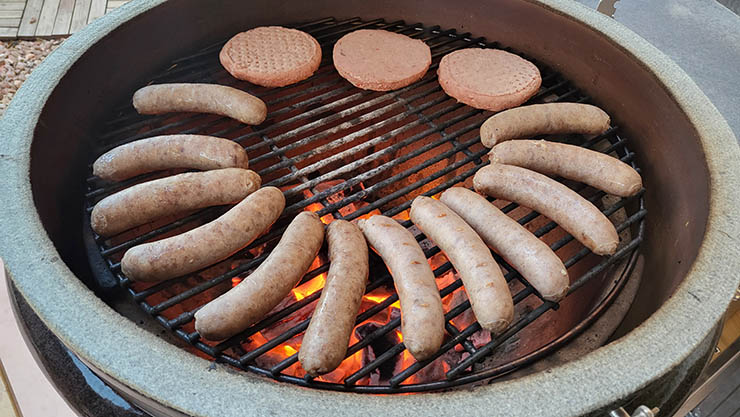 sausages and burgers cooking on the Victory 21-Inch Kamado Grill