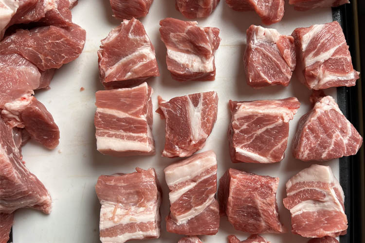 raw pork butt cubes on a white chopping board