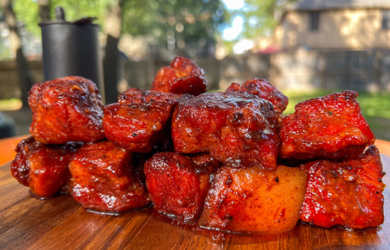 Sticky, caramelized pork butt burnt ends piled on a serving tray with BBQ sauce.