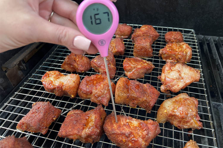 pork butt cubes on the grill with an instant read thermometer in one of them, temp reading 167