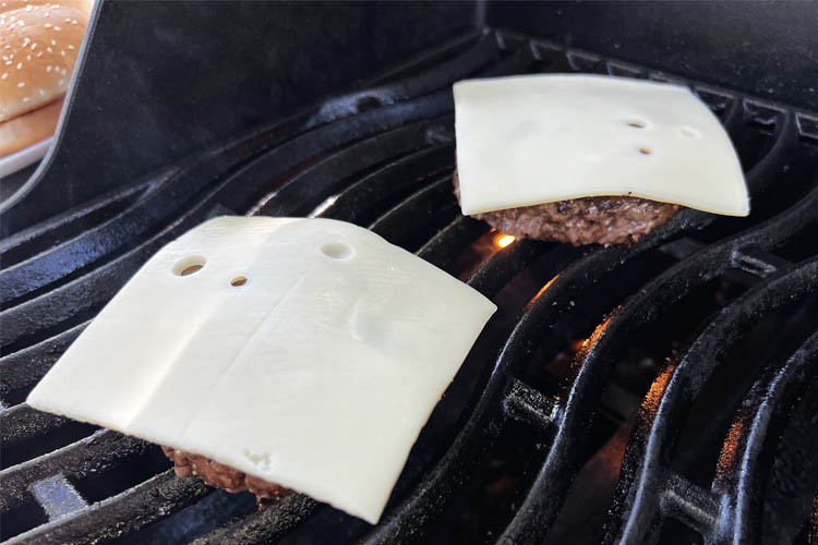 two bison patties on the grill with a slice of swiss cheese on top
