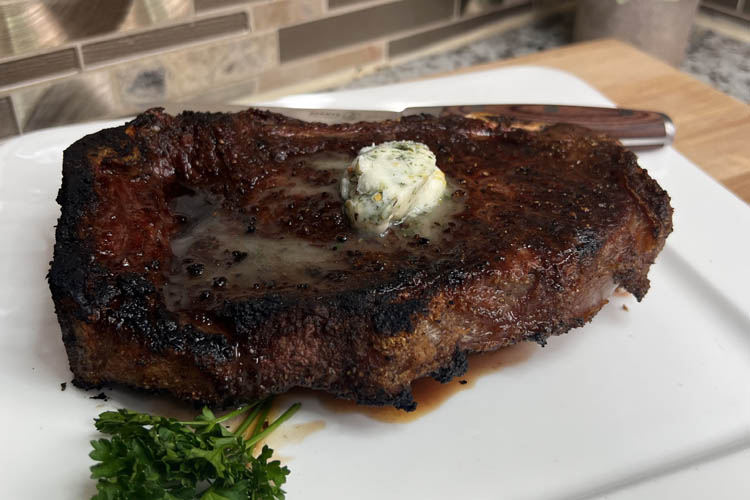 new york strip steak resting on a white plate with a knob of butter on top