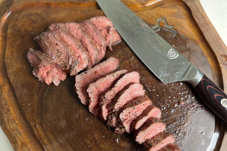 sliced tri-tip on a wooden chopping board with knife alongside