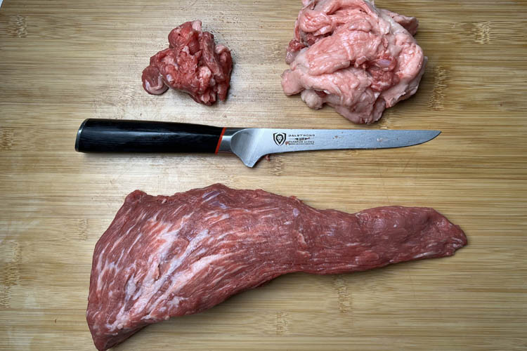 trimmed tritip with a pile of silverskin and the fatcap above it with a knife in the middle