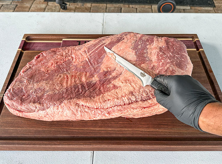 a gloved hand trimming brisket fat with a knife