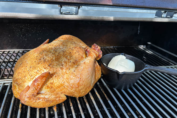 whole chicken on the smoker with a small lodge pot with butter in it