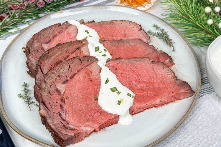 slice of prime rib on a white plate drizzled with horseradish sauce