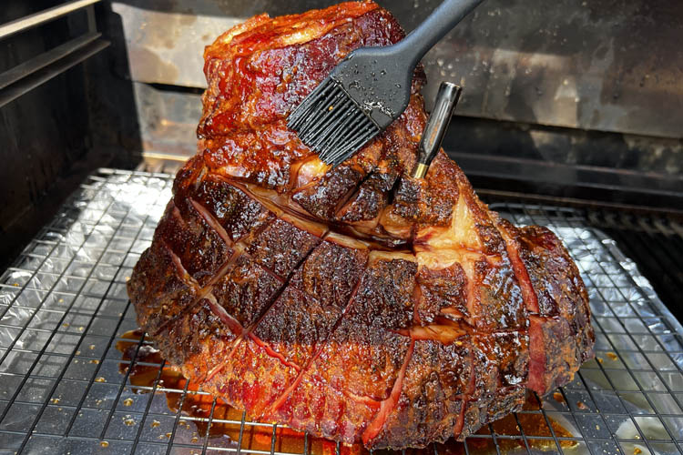 whole ham on the grill being brushed with glaze