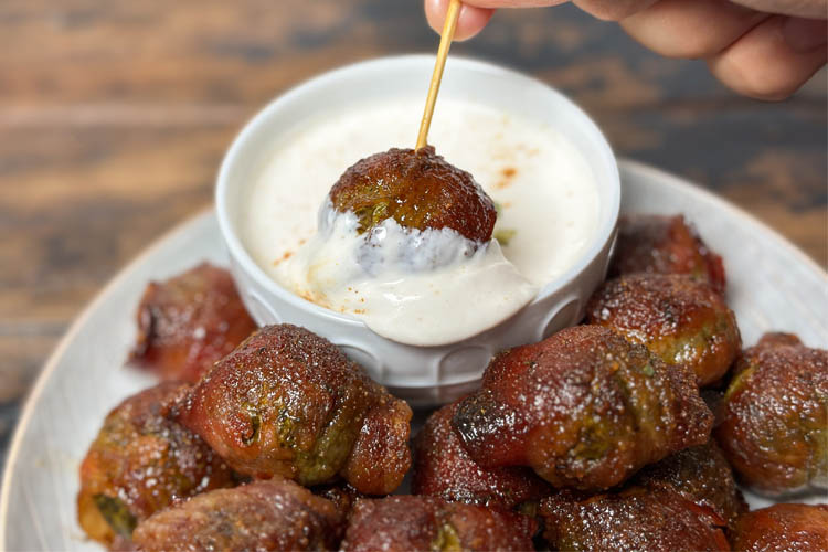 a bacon wrapped brussel sprout on a toothpick being dipped into sauce.