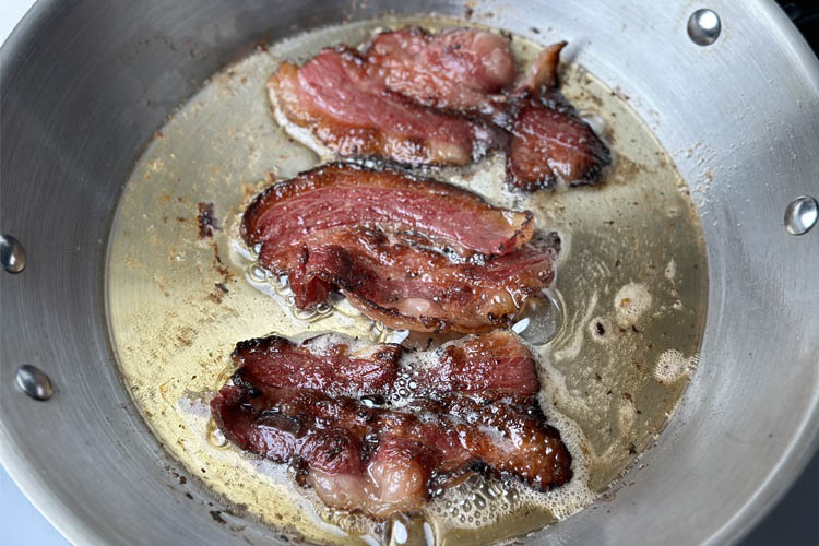 beef bacon frying in oil in frypan