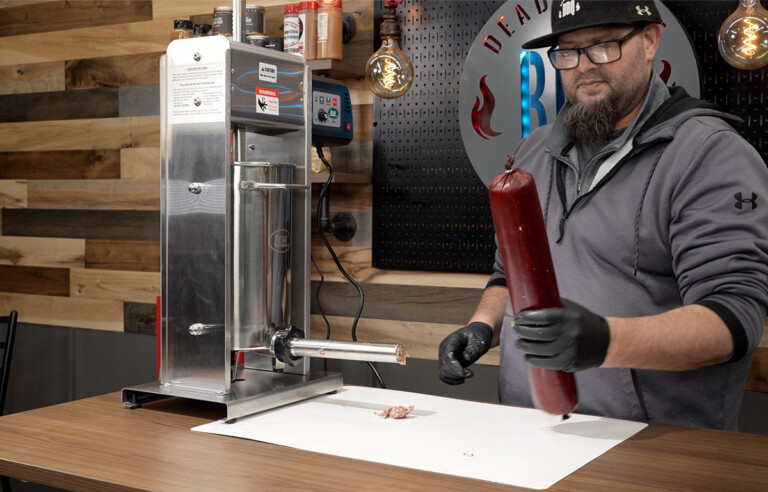 man holding sausage next to LEM sausage stuffer
