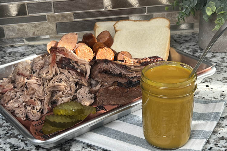 carolina gold sauce in a jar with a platter of meat and bread in the background
