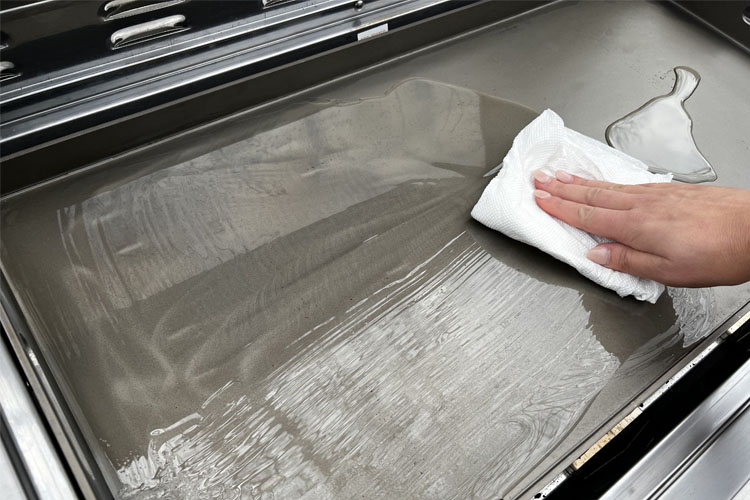 a hand holding a cloth wiping the oil all over the griddle