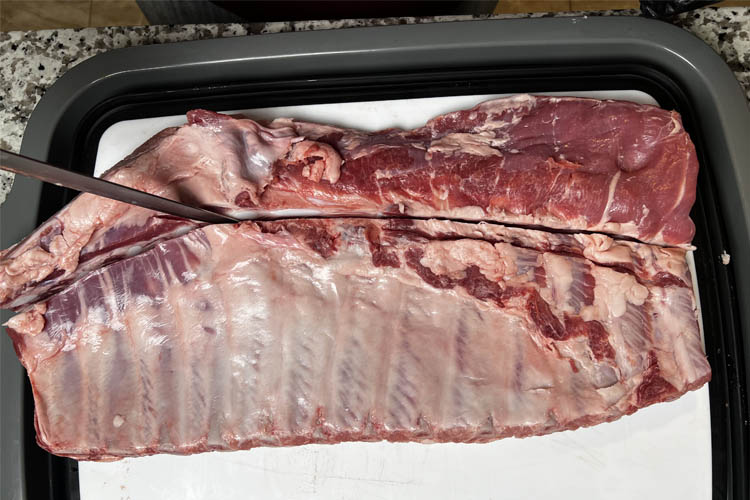 knife cutting through breastbone of pork ribs