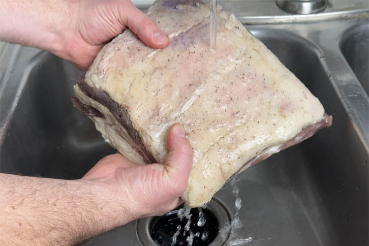 raw beef bacon being washed under a tap