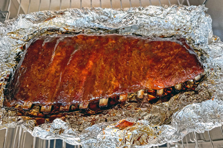 ribs with bbq sauce brushed on them sitting on foil