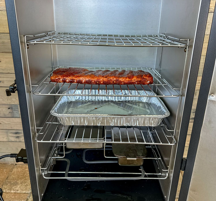 ribs in the electric smoker with a silver tray underneath it
