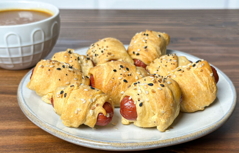 smoked pigs in blanket on a white plate with dipping sauce behind