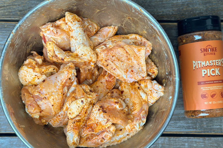raw wings in a bowl with a jar of rub next to it