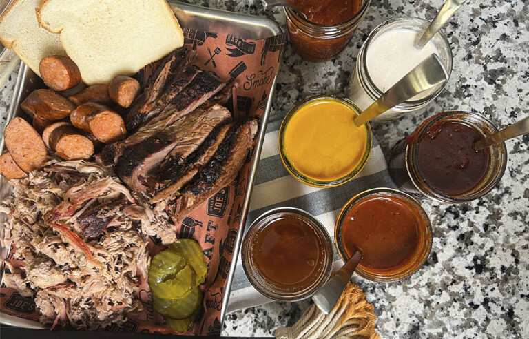 jars of different styles of barbecue sauce next to platter of barbecue meats