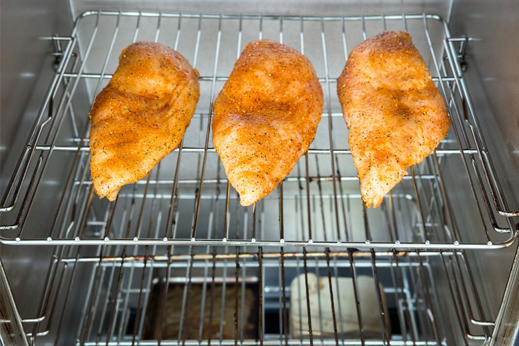 three raw chicken breasts in the electric smoker