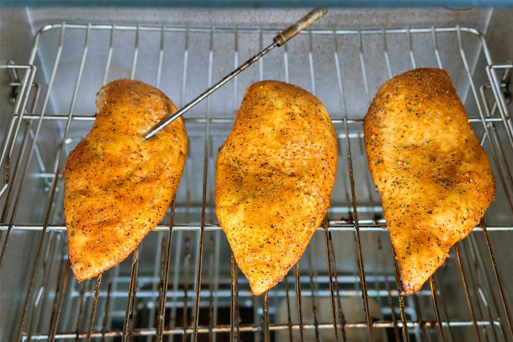 three chicken breasts in the electric smoker, one with a temperature probe in it