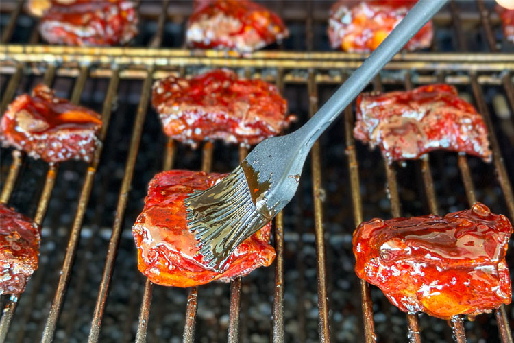 brushing bbq sauce on a rib tip in the grill