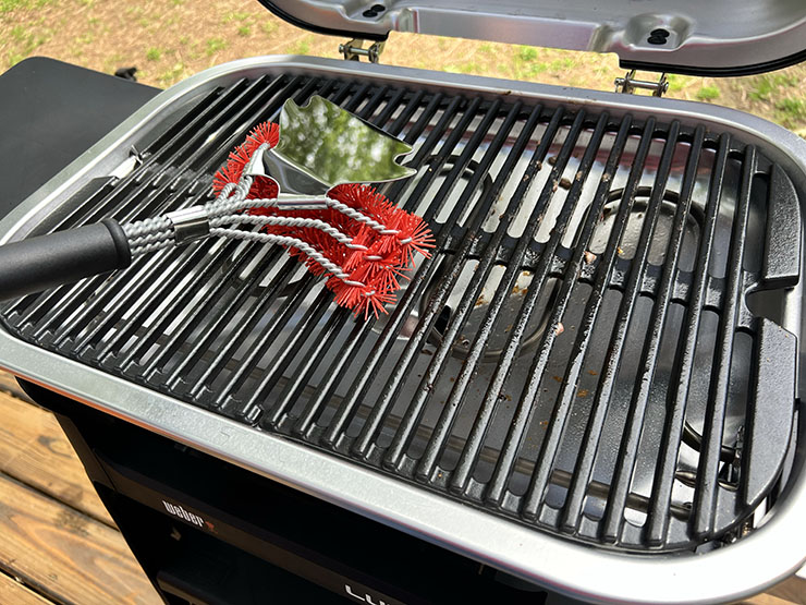 a person cleaning Weber Lumin grill with a grill brush