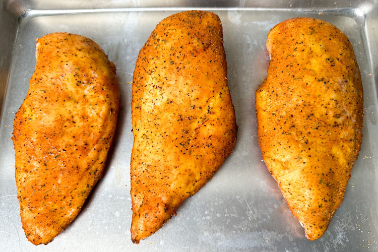 three cooked chicken breasts on a metal tray