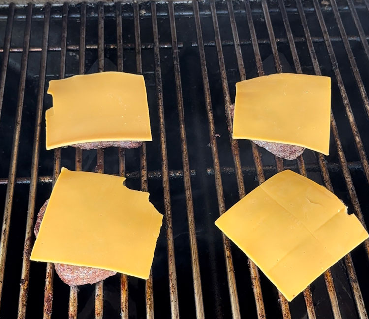 burgers on the grill with a slice of cheese on top
