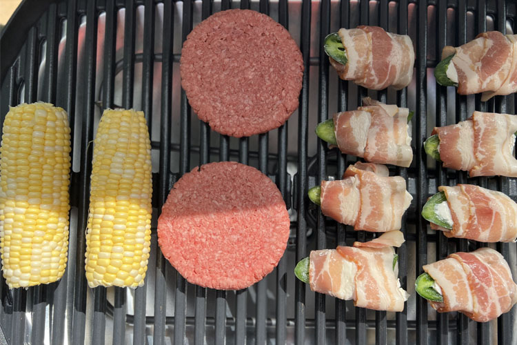 corn, burger patties and jalapeno poppers on a grill