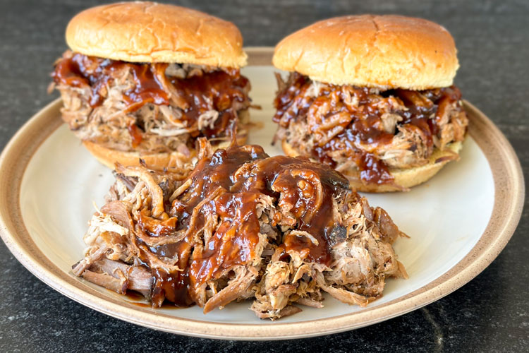 shredded pulled pork with bbq sauce and two burgers in the background