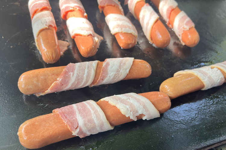 bacon-wrapped hot dogs on the griddle
