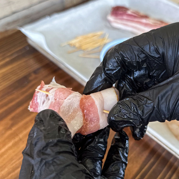 hand securing a toothpick in a bacon wrapped shrimp