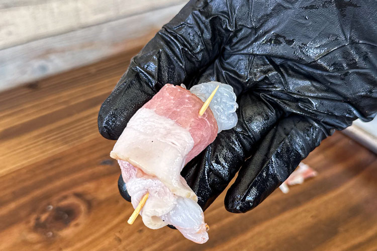 hand hold raw bacon wrapped shrimp with toothpick