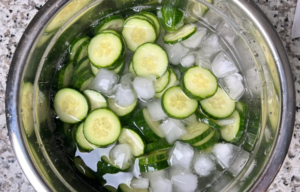 sliced cucembers in water and ice in a metal bowl