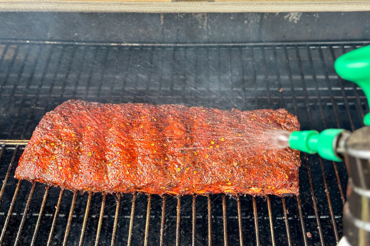 ribs on grill being spritzed