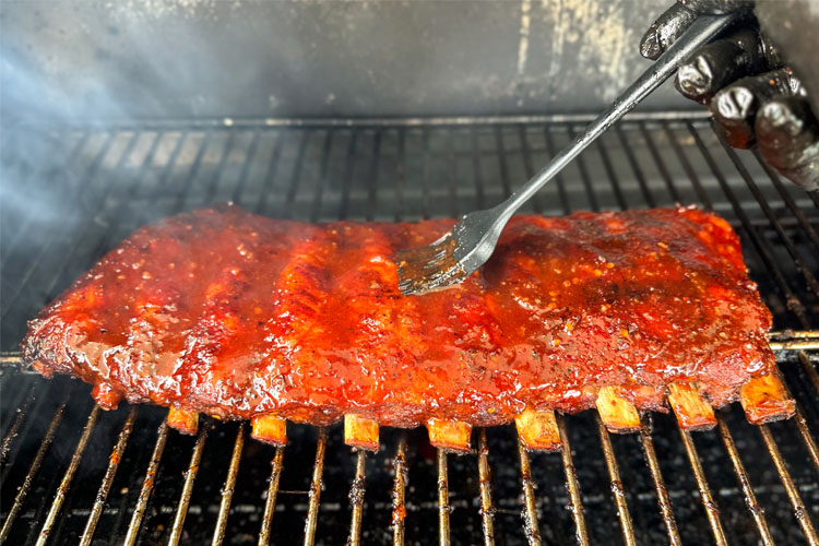 ribs on the grill being brushed with glaze