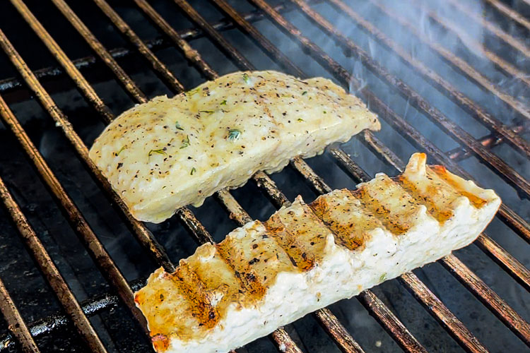 two pieces of halibut on the grill, one has been flipped