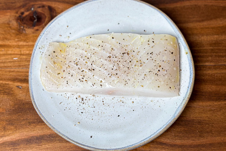 a piece of raw sesoned halibut on a white plate