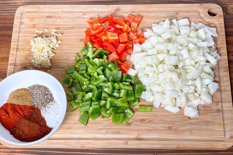chopped veges and a bowl of spice on a wooden chopping board